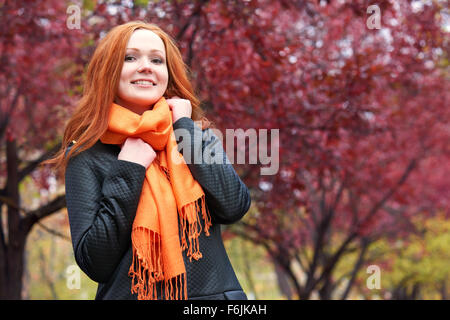 Redhead ragazza nel parco della città sulla struttura ad albero rosso sfondo, caduta stagione Foto Stock