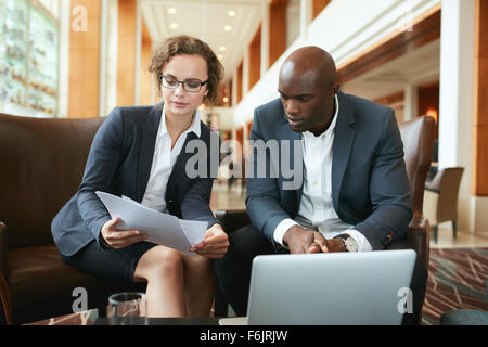 Ritratto di giovane donna e uomo seduto nella lobby dell'albergo a discutere di carte. La gente di affari riuniti in coffee shop readin Foto Stock