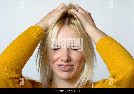 Vicino la giovane donna di graffiare la sua testa con due mani, mostrando disgustato espressione facciale, contro sfondo grigio chiaro. Foto Stock