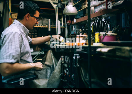 Lavoratore lavora in officina circondato dai suoi strumenti Foto Stock