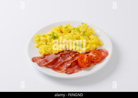Piatto di uova strapazzate e fette di pancetta fritta su sfondo bianco Foto Stock
