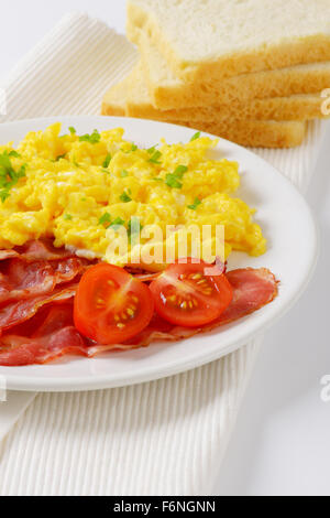 Piatto di uova strapazzate e pancetta fritta e fette di pane sul posto bianco mat Foto Stock