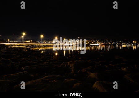 Lungo litorale innevato con luce riflettendo sulla superficie con tromsoe città illuminazione notturna in background Foto Stock