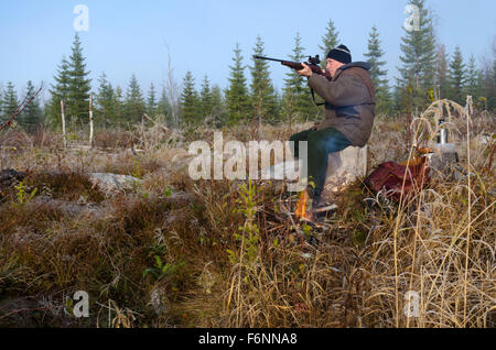 Moose hunter seduti su un moncone con un po' incendio nel puntamento frontale con un fucile, immagine dal nord della Svezia. Foto Stock