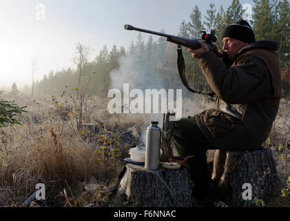 Moose hunter seduti su un moncone con un po' fumoso fuoco nel puntamento frontale con un fucile e con un sandwich e un thermos in attesa. Foto Stock