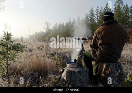 Moose hunter seduti su un moncone con un po' fumoso fuoco davanti tenendo un fucile , immagine dal nord della Svezia. Foto Stock