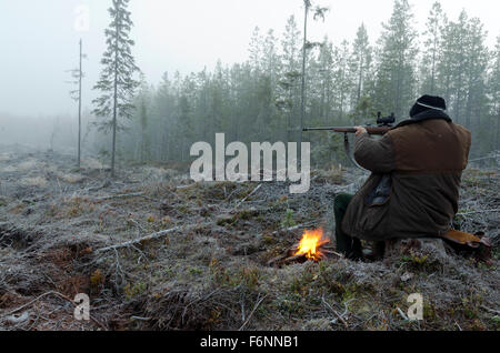 Moose hunter seduti su un moncone con un po' di fuoco nel puntamento frontale con un fucile, immagine dal nord della Svezia. Foto Stock