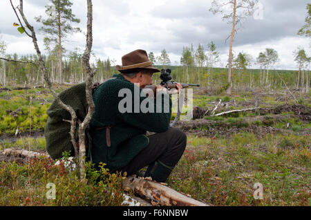 Moose hunter seduto su un moncone mirando con un fucile, immagine dal nord della Svezia. Foto Stock