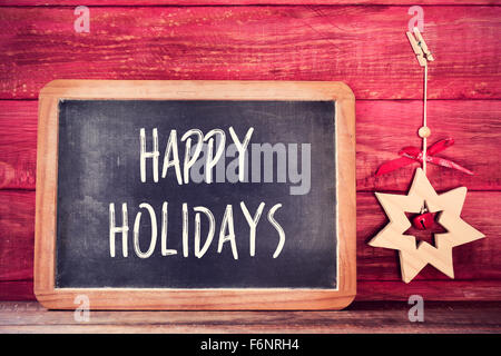 Una lavagna con il testo Happy Holidays scritto in esso e un di legno stella di natale su un rustico rosso superficie in legno Foto Stock