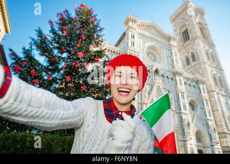 Donna turistico con bandiera italiana di sorridere mentre prendendo selfie nella parte anteriore del tradizionale albero di natale vicino al Duomo di Firenze. Chris Foto Stock