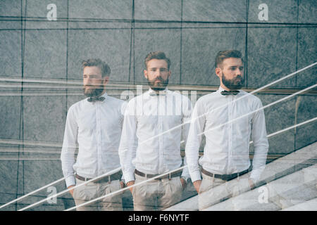 Tripla esposizione di una giovane bella capelli biondi uomo caucasico guardando a destra nella fotocamera e a sinistra e con le mani in tasca, appoggiato contro una parete - creative, il concetto di arte Foto Stock