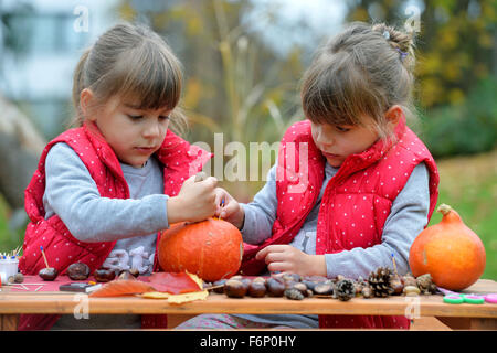 Due gemelle creando divertenti figure fuori di zucca, castagno e foglie. Foto Stock