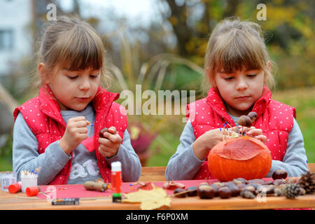 Due gemelle creando divertenti figure fuori di zucca, castagno e foglie. Foto Stock