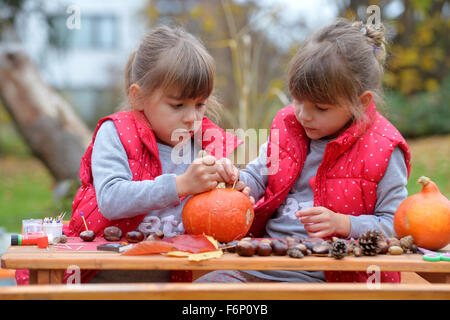 Due gemelle creando divertenti figure fuori di zucca, castagno e foglie. Foto Stock