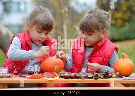 Due gemelle creando divertenti figure fuori di zucca, castagno e foglie. Foto Stock