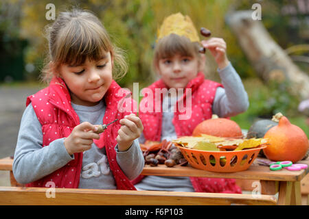 Due gemelle creando divertenti figure fuori di zucca, castagno e foglie. Foto Stock