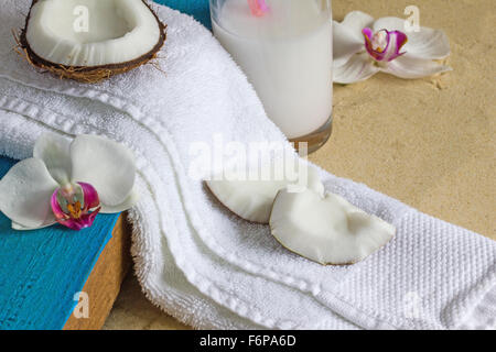 Il relax in spiaggia con noce di cocco, orchidee, latte di cocco, asciugamano bianco e aqua legno dipinto su un sfondo sabbia. Copyspace Foto Stock