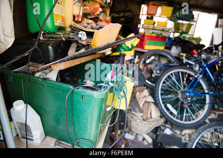 All'interno di un confuso e ingombra di garage in legno capannone con strumenti, biciclette e attrezzature da giardino ammucchiati sui ripiani irregolare Foto Stock