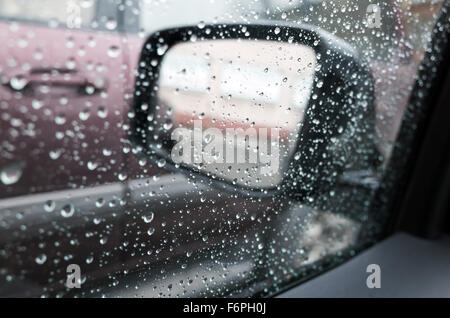 Wet finestra auto con gocce di pioggia e uno specchio dietro. Primo piano con messa a fuoco selettiva e DOF poco profondo Foto Stock