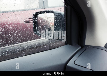 Wet finestra auto con gocce di pioggia e uno specchio dietro. Close-up foto con messa a fuoco selettiva e DOF poco profondo Foto Stock