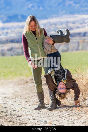 Attraente madre scherzosamente mentre tiene il suo giovane figlio capovolta lungo il percorso di sporcizia sul ranch Foto Stock
