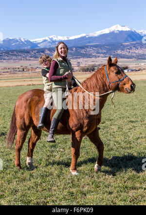 Attraente la madre e il giovane figlio di equitazione nel ranch dei pascoli Foto Stock