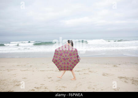 Donna che cammina con ombrellone in spiaggia Foto Stock