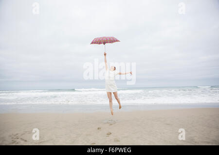 Donna che gioca con ombrellone in spiaggia Foto Stock