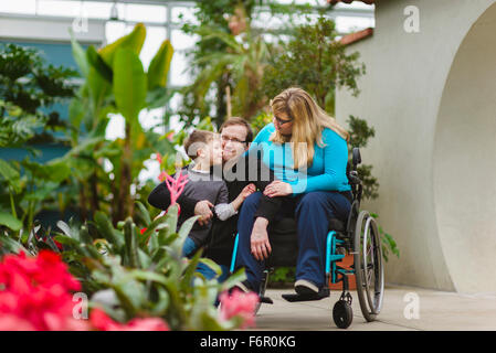 Donna paraplegici e abbracciando la famiglia in giardino Foto Stock