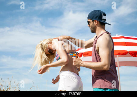 Uomo di applicare una lozione solare su una donna indietro Foto Stock