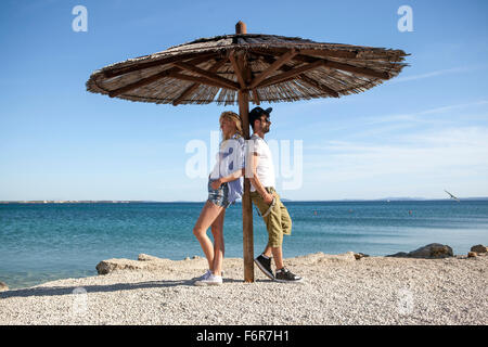 Coppia giovane in piedi sotto ombrellone in spiaggia Foto Stock