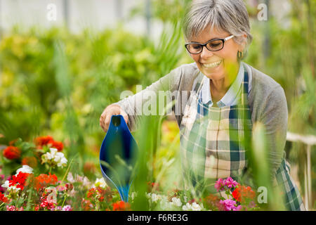 Bella donna matura in un giardino di fiori di irrigazione Foto Stock