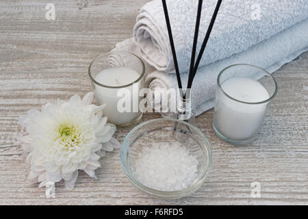 Composizione Spa con asciugamani bianchi, candele, fiori, bastoncini di incenso e di sale da bagno sul tavolo di legno Foto Stock