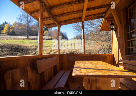 Veranda in Legno, veranda di una piccola casa di montagna. Il sole splende e il cielo è blu chiaro. Foto Stock