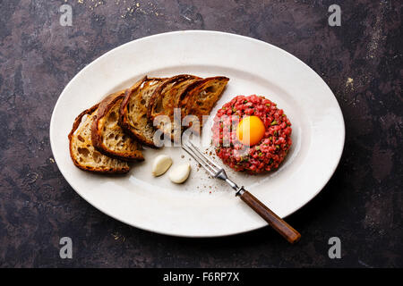 Tartare di manzo con cetriolo sottaceto e toast sulla piastra bianca su sfondo scuro Foto Stock