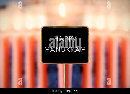 Primo piano di una lavagna con testo Happy Hanukkah e una menorah con nove candele accese in background Foto Stock