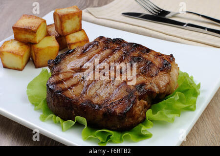 Pezzo di succosa bistecca di carne di maiale alla griglia con patate arrosto Foto Stock