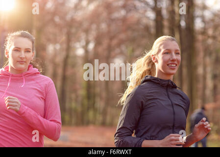 Due attraenti montare le giovani signore jogging insieme attraverso una foresta di autunno in chat come essi corrono attraverso gli alberi, in un healt Foto Stock