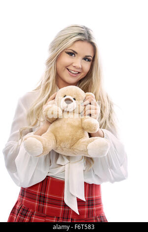 Bella bionda gioca con Teddy bear.La bambina indossa una gonna scozzese rosso colore saturo e una camicetta bianca.ragazza baciare un giocattolo Foto Stock