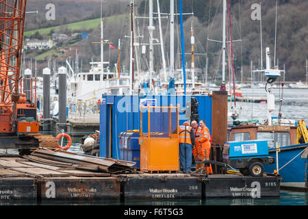Operai indossando "hi-viz' abbigliamento lavorare su una costruzione galleggiante piattaforma di lavoro in Dartmouth Harbour. Foto Stock