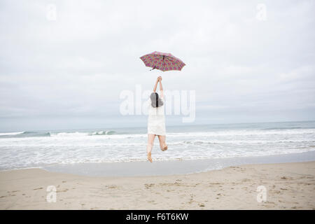 Donna che gioca con ombrellone in spiaggia Foto Stock