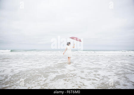 Donna wading con ombrellone in spiaggia Foto Stock