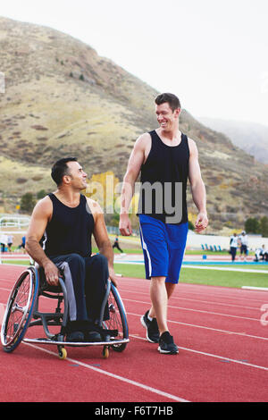 Atleta paraplegico in sedia a rotelle con un amico sulla via Foto Stock