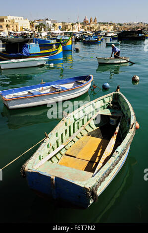 Il vecchio uomo in piedi su una piccola barca con molte altre barche intorno al porto di Marsaxlokk, Malta Foto Stock