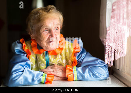 Vecchia donna in slavo costume etnico siede a un tavolo vicino alla finestra. Foto Stock