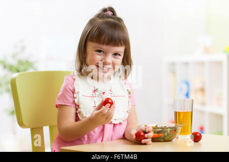 La ragazza del bambino che mangia la cena e mostra i pomodori Foto Stock