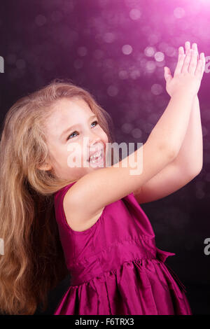 Poco carino ragazza in un abito rosa su sfondo nero in studio Foto Stock