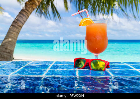 Cocktail di arancione e occhiali da sole, sul bordo della piscina a sfioro Foto Stock