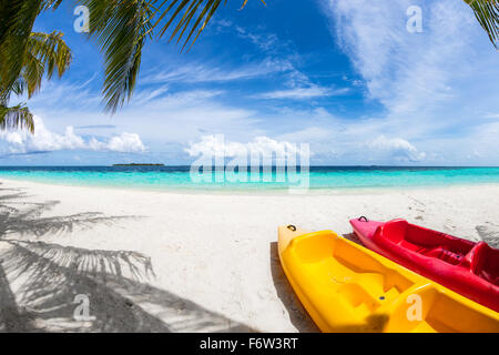 Il rosso e il giallo kayak sulla spiaggia sotto le palme di cocco Foto Stock