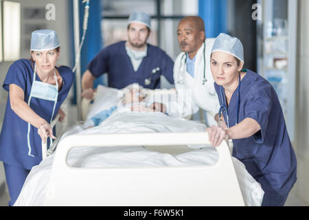 I medici spingendo un letto con paziente Foto Stock